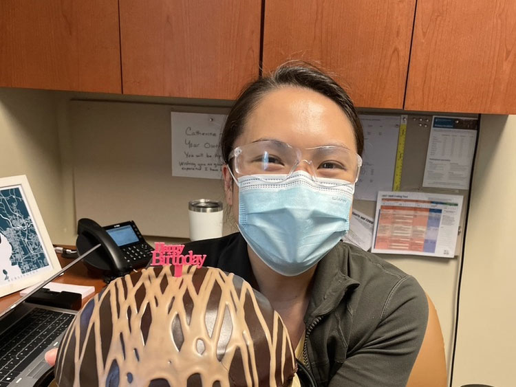 A photo of Catherine Vu Morrisey holding a birthday cake while in a face mask and lab goggles.