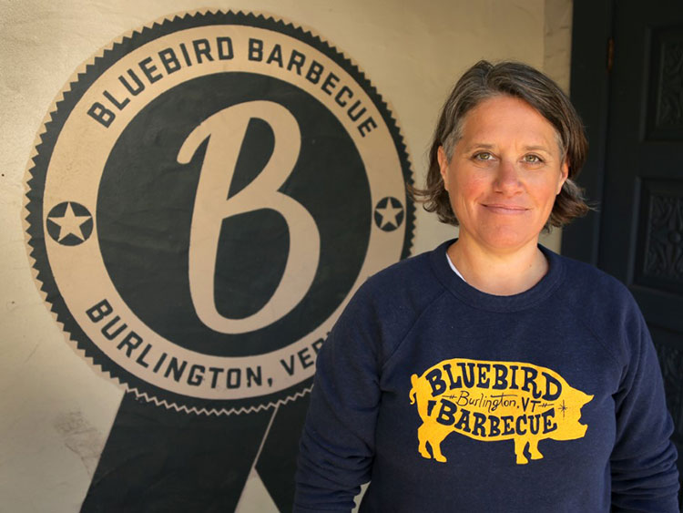 A photo of Sue Bette in front of her business logo, Bluebird Barbecue.
