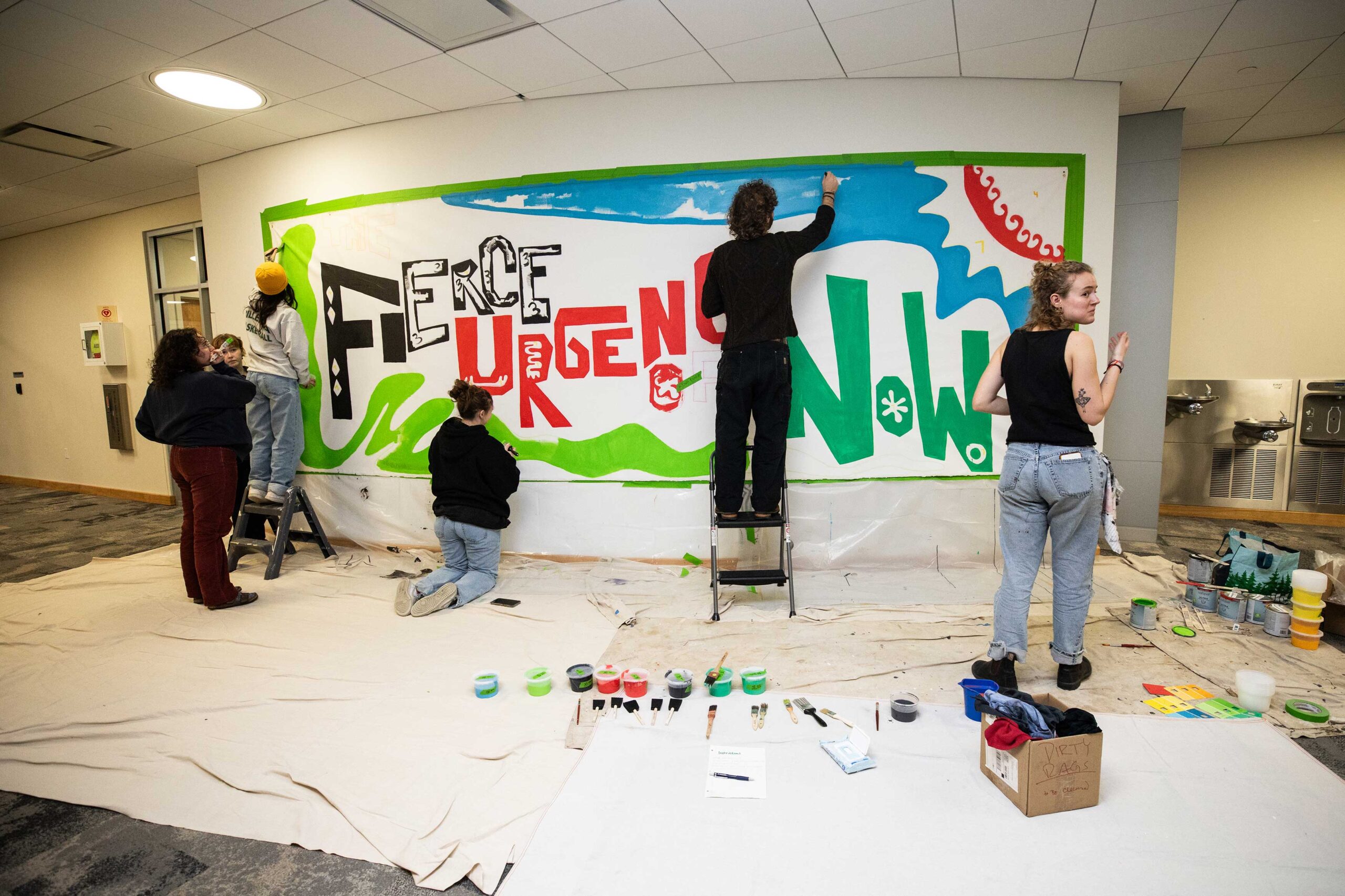 students painting a mural that reads "fierce urgency now"