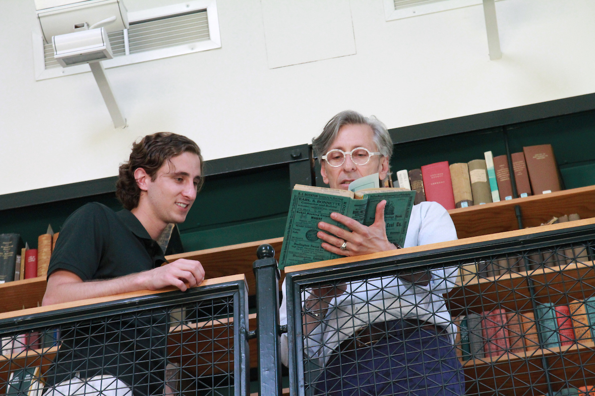 a male student and Professor Mike Bosia look at book together in the library's special collections room.